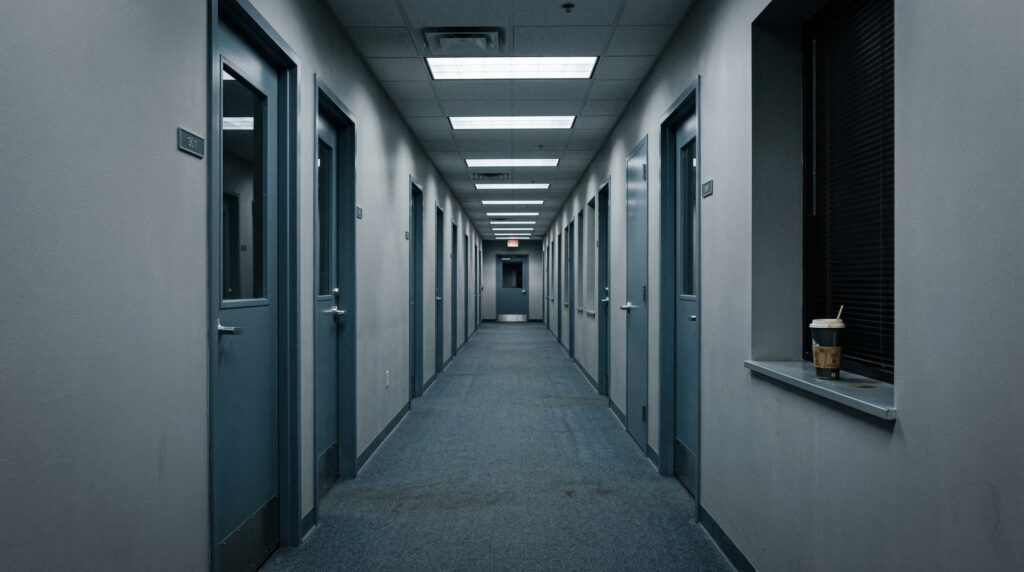 Lawyer for hostile work environment — empty corporate office hallway with harsh fluorescent lighting and closed doors